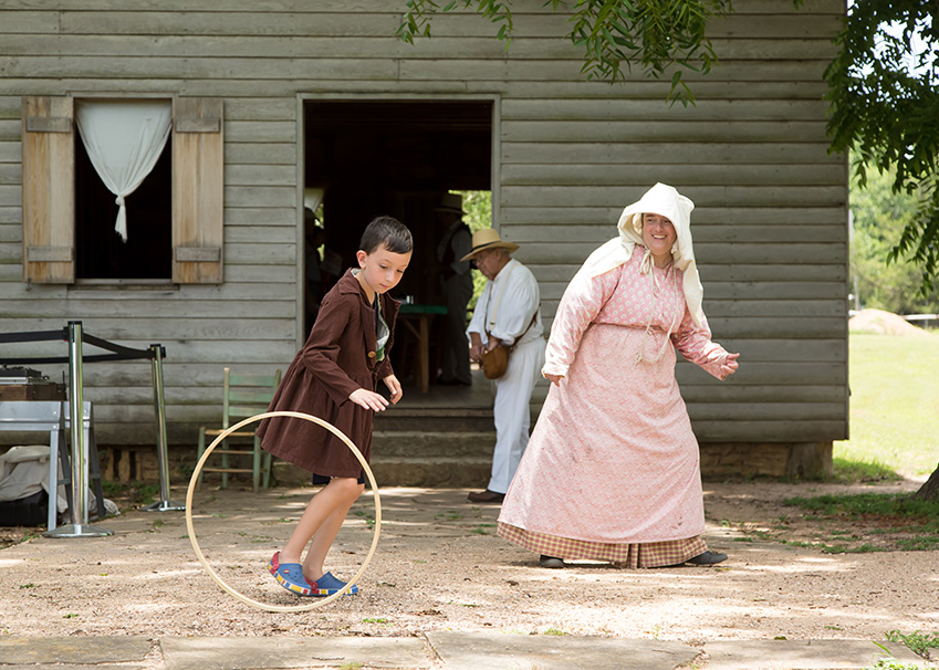 A young boy playing a game with a women. They are both dressed in old timey clothing.