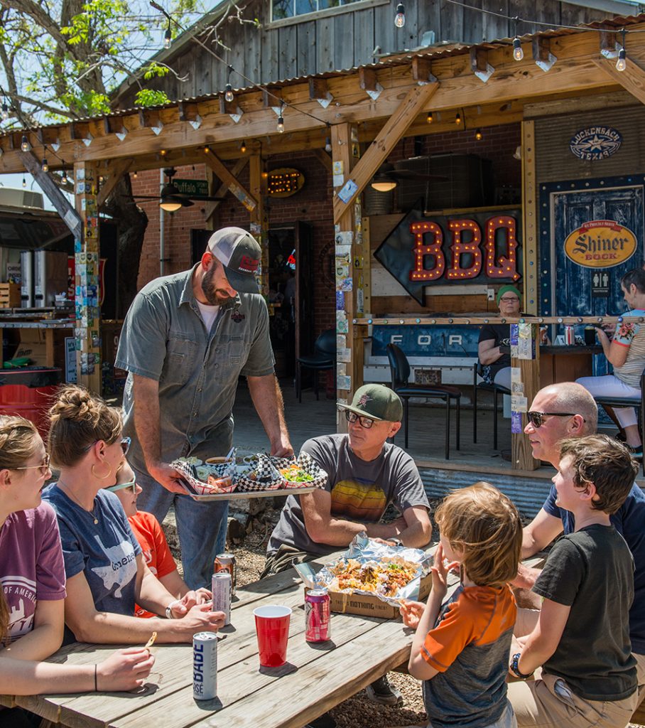A man serving BBQ to a group of people sitting outside at a table at Pioneer BBQ.