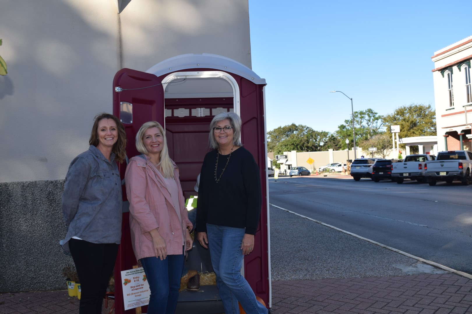 Three women standing in front of a porta potty for the scarecrow extravaganza.