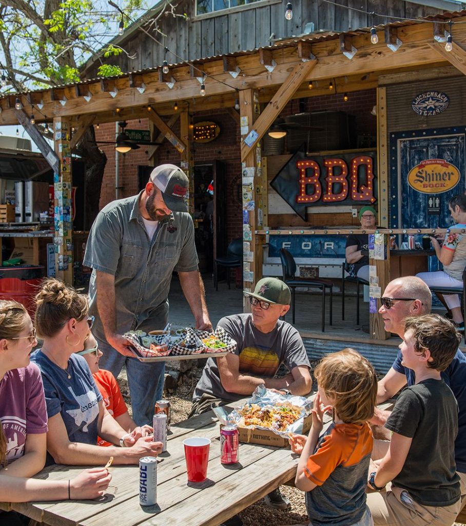 Man serving bbq to a group of people sitting outside at a table at Pioneer BBQ
