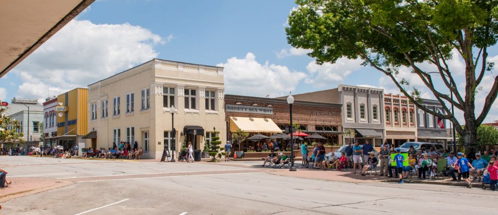 People lining the sidewalks of downtown Brenham in anticipation of a parade.