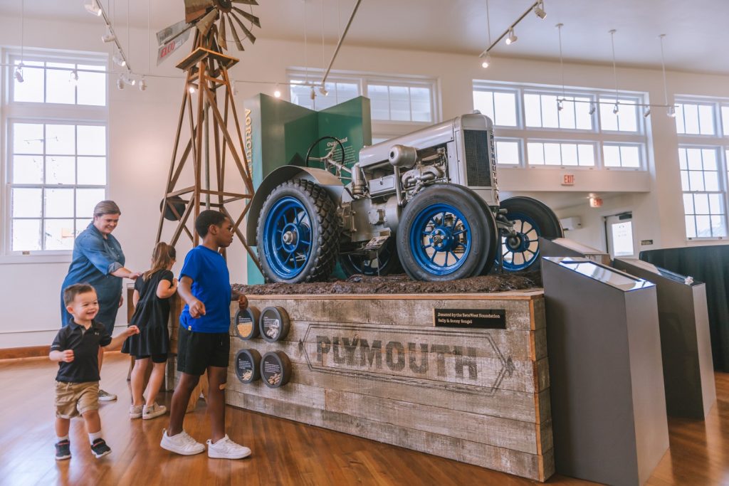 Three children and their mom are all looking at a vehicle in the exhibit. Brenham Heritage Museum