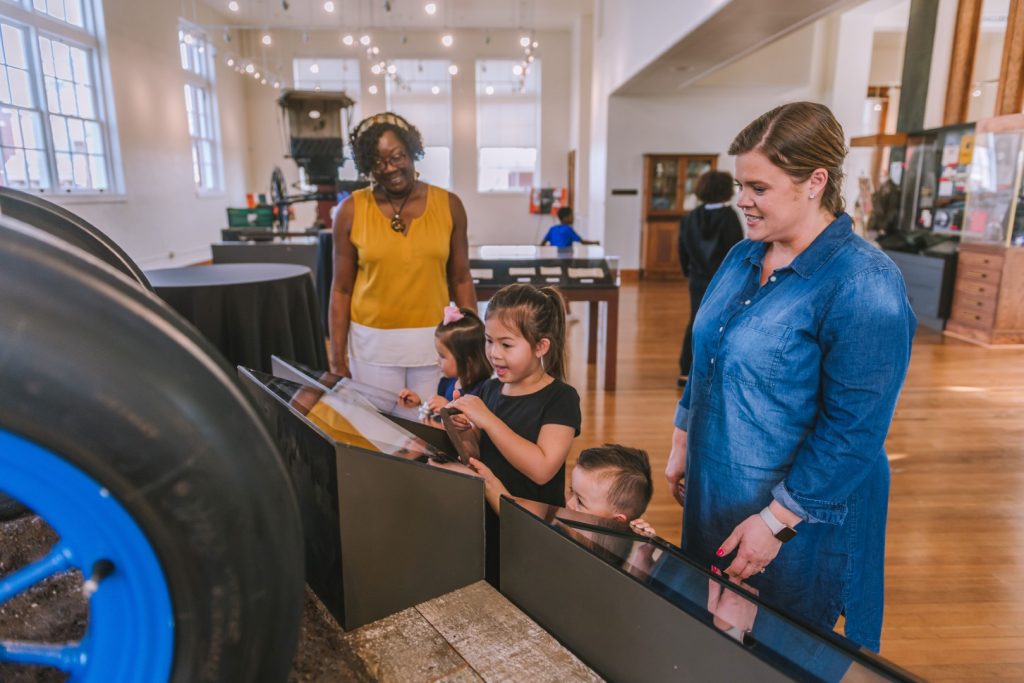 Two women and three children all look at a display of the exhibit together.