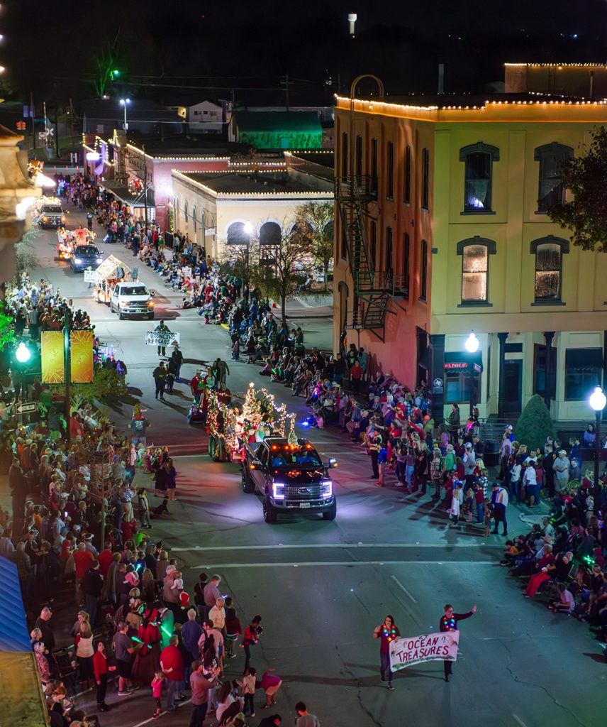Lighted Christmas Parade in Downtown Brenham with crowds of people on either side of the street and floats in the street.