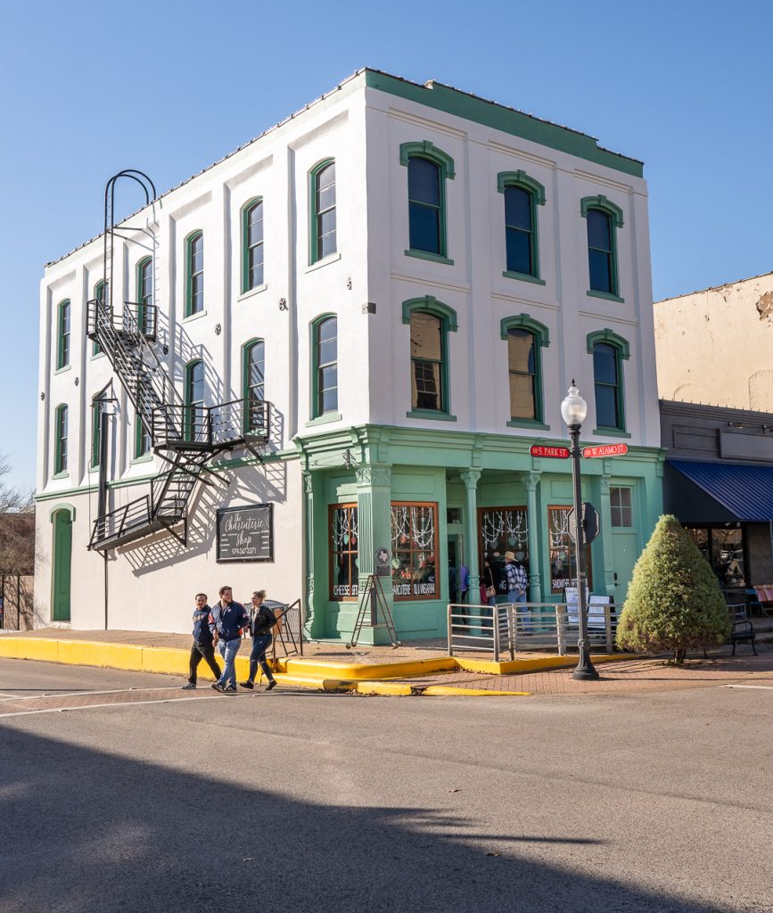 Uptown Swirl participants on a sunny day in Downtown Brenham. A historic three-story building is in the background as a group of shoppers cross the street.