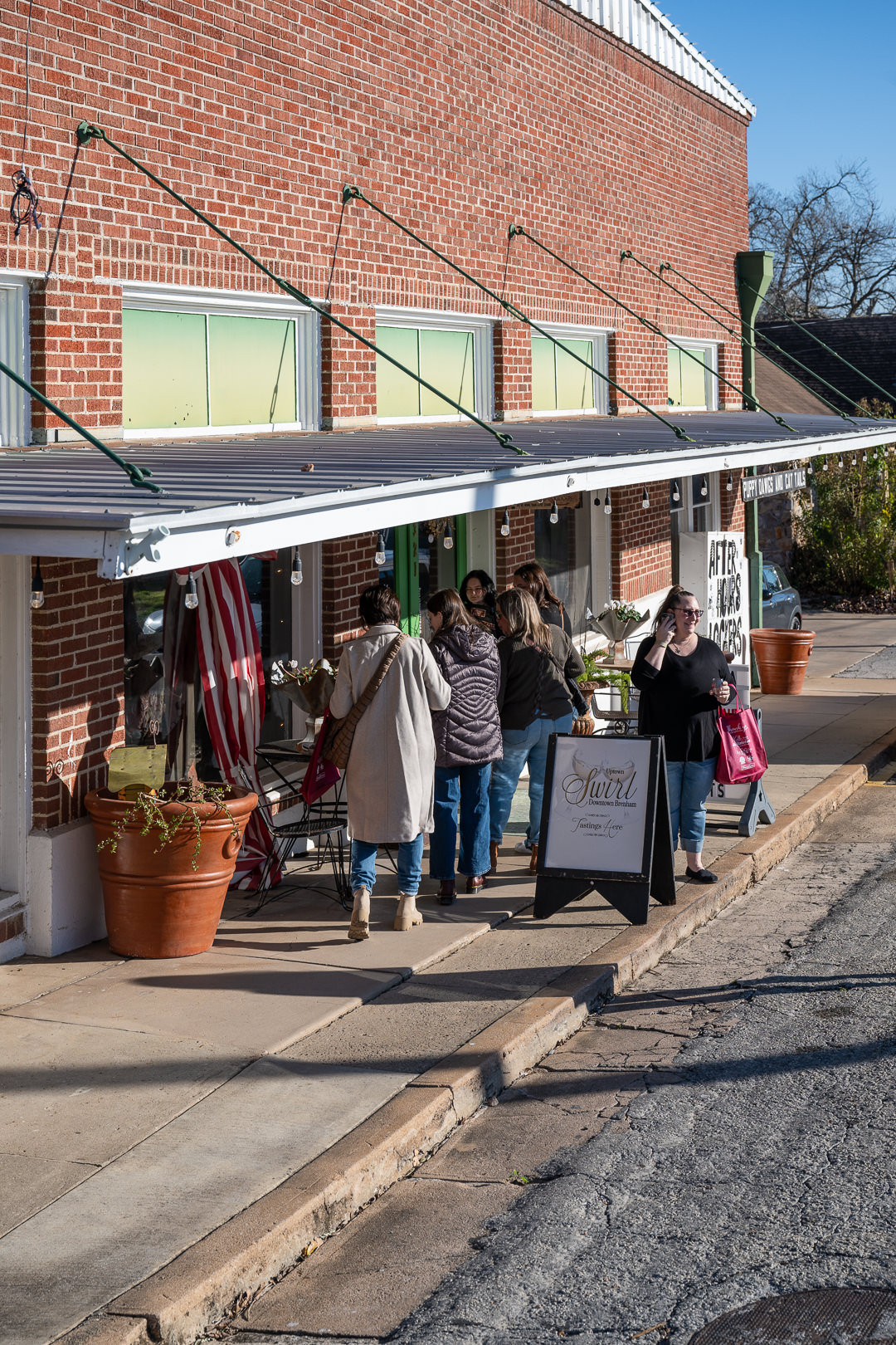 Uptown Swirl participants are gathered to look at items on the porch at Puppy Dawgs and Cat Tails on a sunny day in Downtown Brenham.