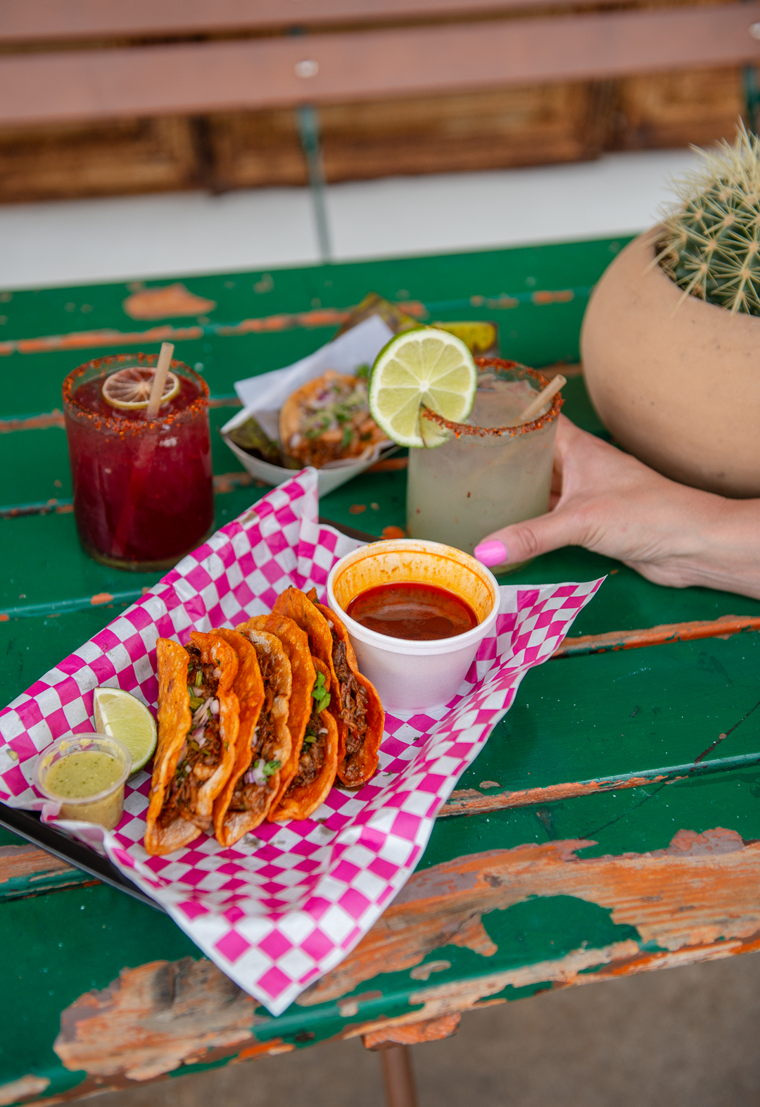 A platter of birria tacos, with a hand holding a margarita.