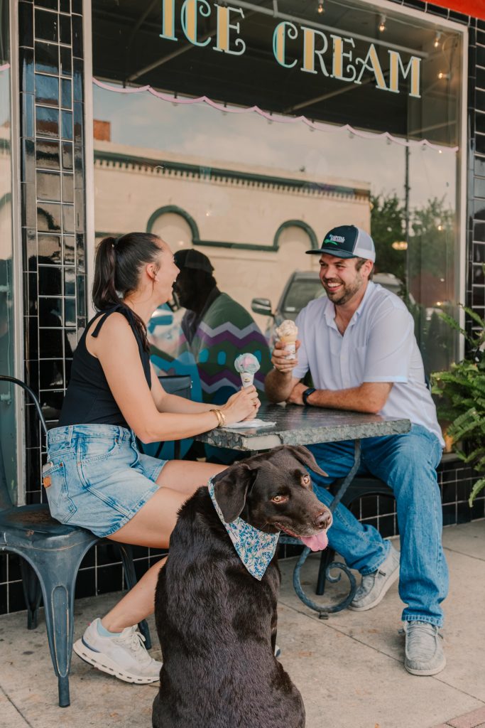 A couple sitting on the patio at Must Be Heaven eating ice cream. There is a brown dog sitting at their side.