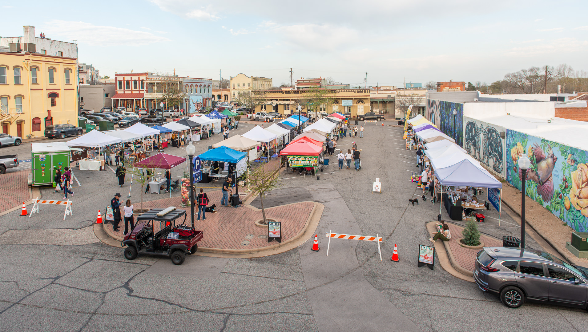 with a backdrop of historic buildings and modern murals, shoppers stroll at the First Friday Farmer & Artisan Market in Downtown Brenham